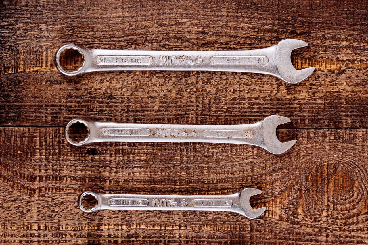 Three metallic wrenches arranged on a rustic wooden table, top view.